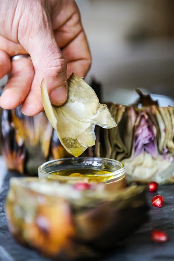 Artichoke leaves being dipped into sauce by a hand