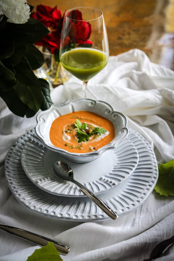 bowl of vegan curried cauliflower soup in a white bowl on two white plates garnished with white cream and cilantro leaves