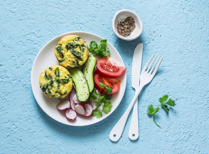 mini frittatas with lacinato kale and shallots on a white plate with a salad on a blue table with knife and fork