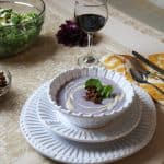 Simple Cauliflower Soup with Sundried Tomato Tapenade in a bowl on two white plates with a glass of wine