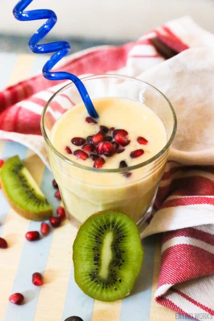 mango smoothie in a glass with a blue straw with pomegranates and kiwi