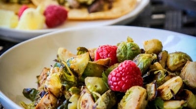 sautéed brussels sprouts in a white bowl with raspberries on top