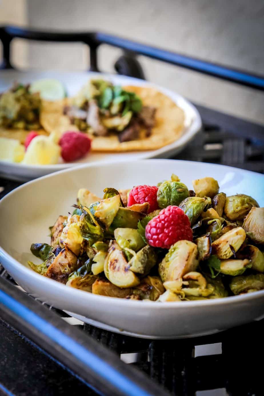 sautéed brussels sprouts in a white bowl with raspberries on top