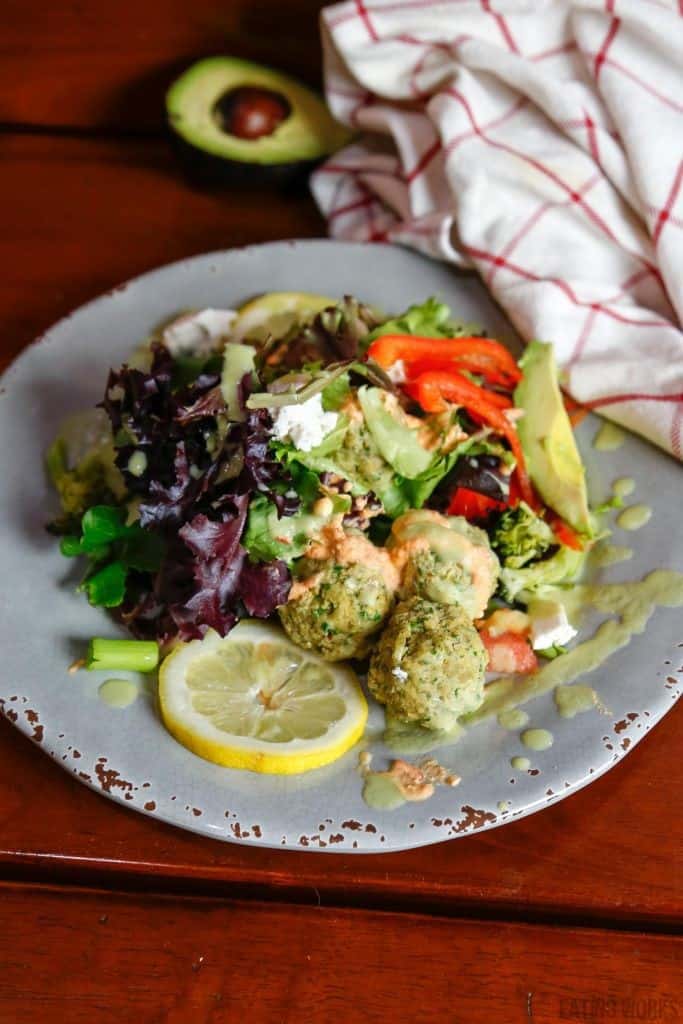 three gluten-free falafel recipe balls on a grey plate with lemon and salad