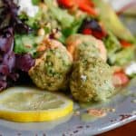 three gluten-free falafel balls on a grey plate with lemon and salad