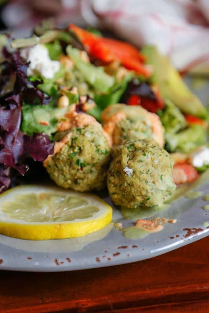 three gluten-free falafel recipe balls on a grey plate with lemon and salad