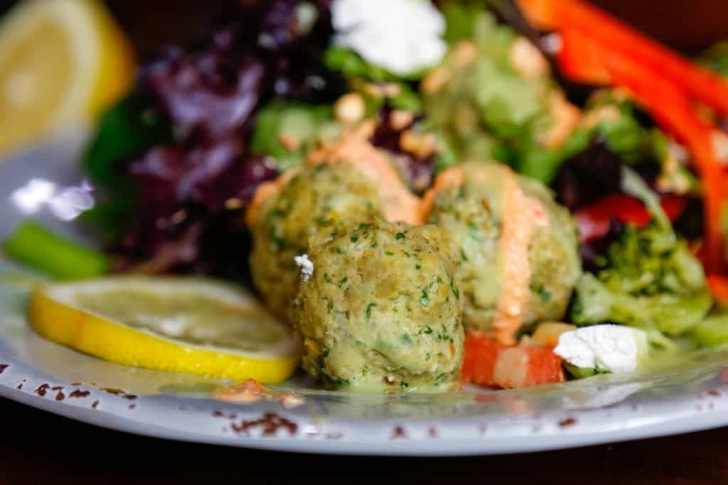 three gluten-free falafel balls on a grey plate with lemon and salad