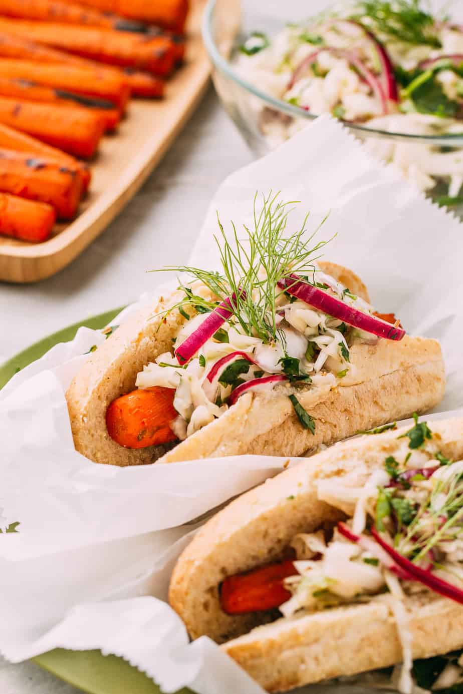 vegan carrot dogs in a hot dog bun topped with sprouts and white sauce