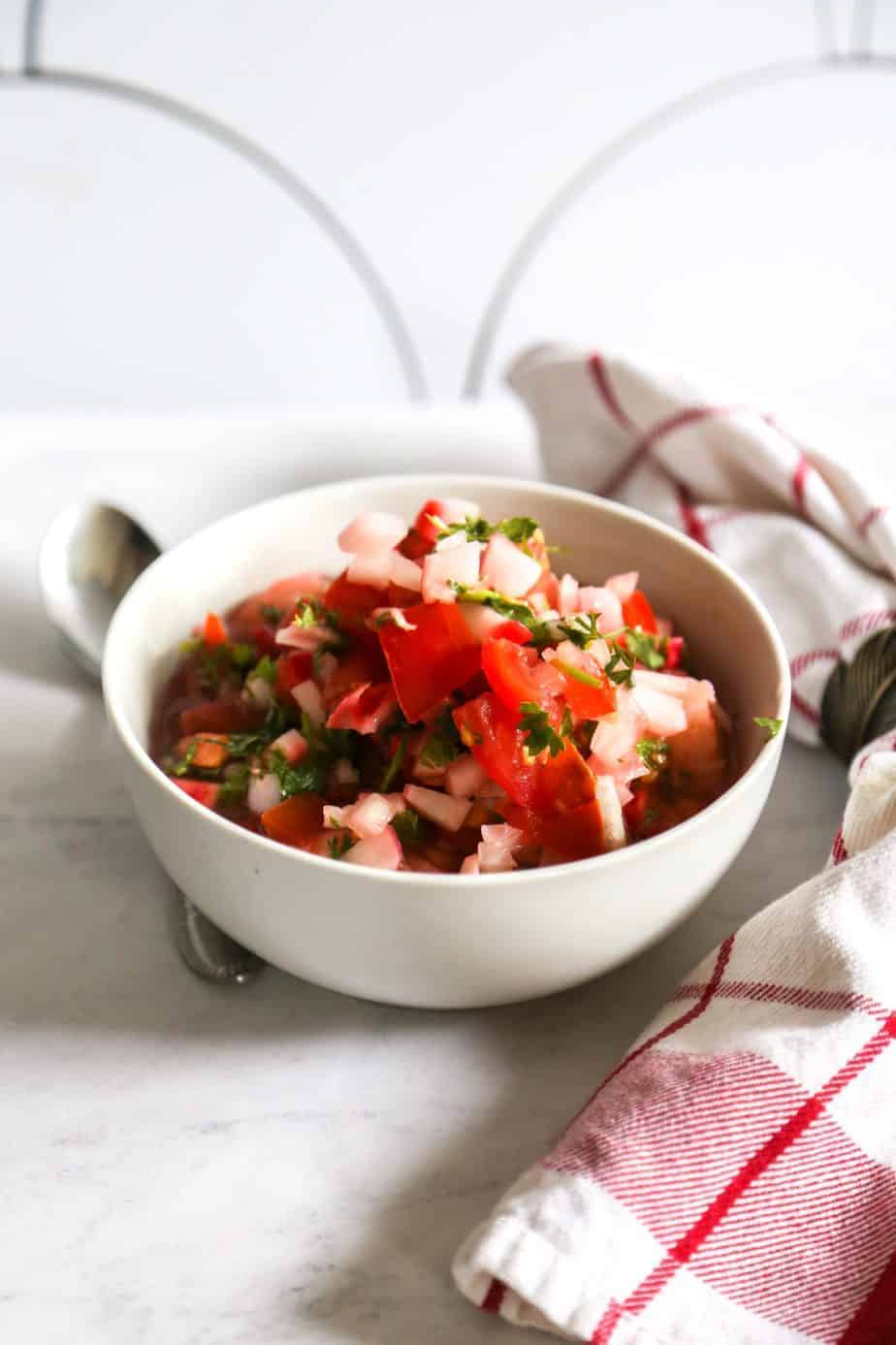 Bowl of shrimp ceviche with tomatoes with a white and red napkin and spoon