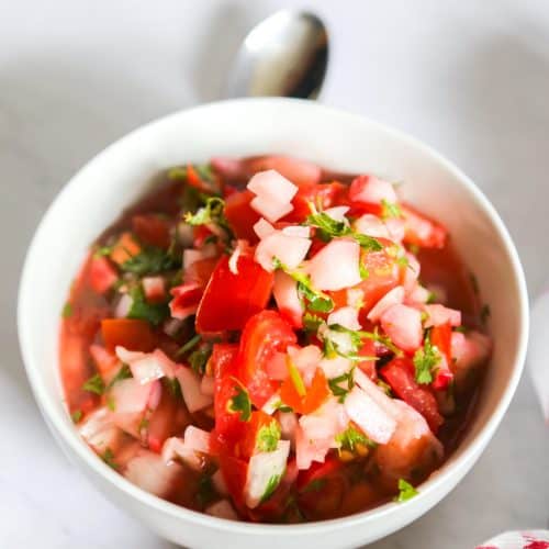 Bowl of shrimp ceviche with tomatoes with a white and red napkin and spoon