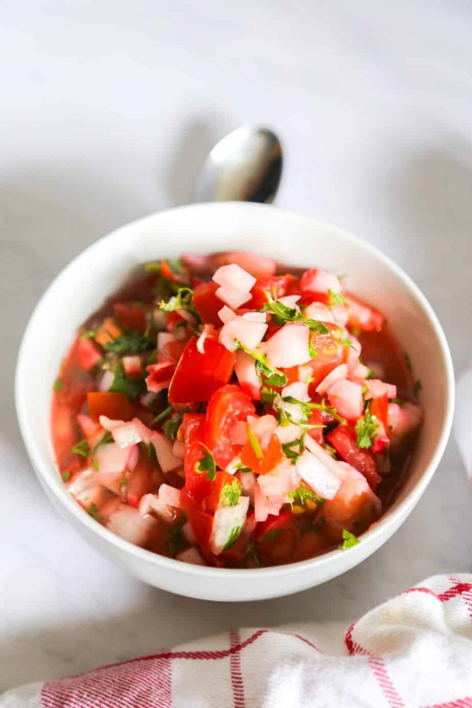 Bowl of shrimp ceviche with tomatoes with a white and red napkin and spoon