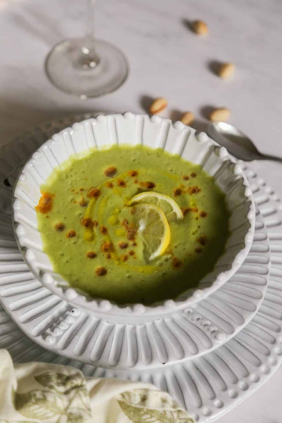 cold cucumber soup garnished with lemons in a white bowl on a white plate with a napkin