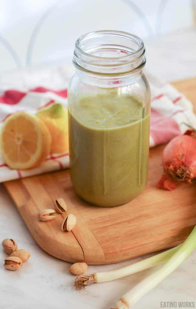 a jar of dairy free Ceasar dressing on a cutting board with lemons scallions nuts and a table cloth