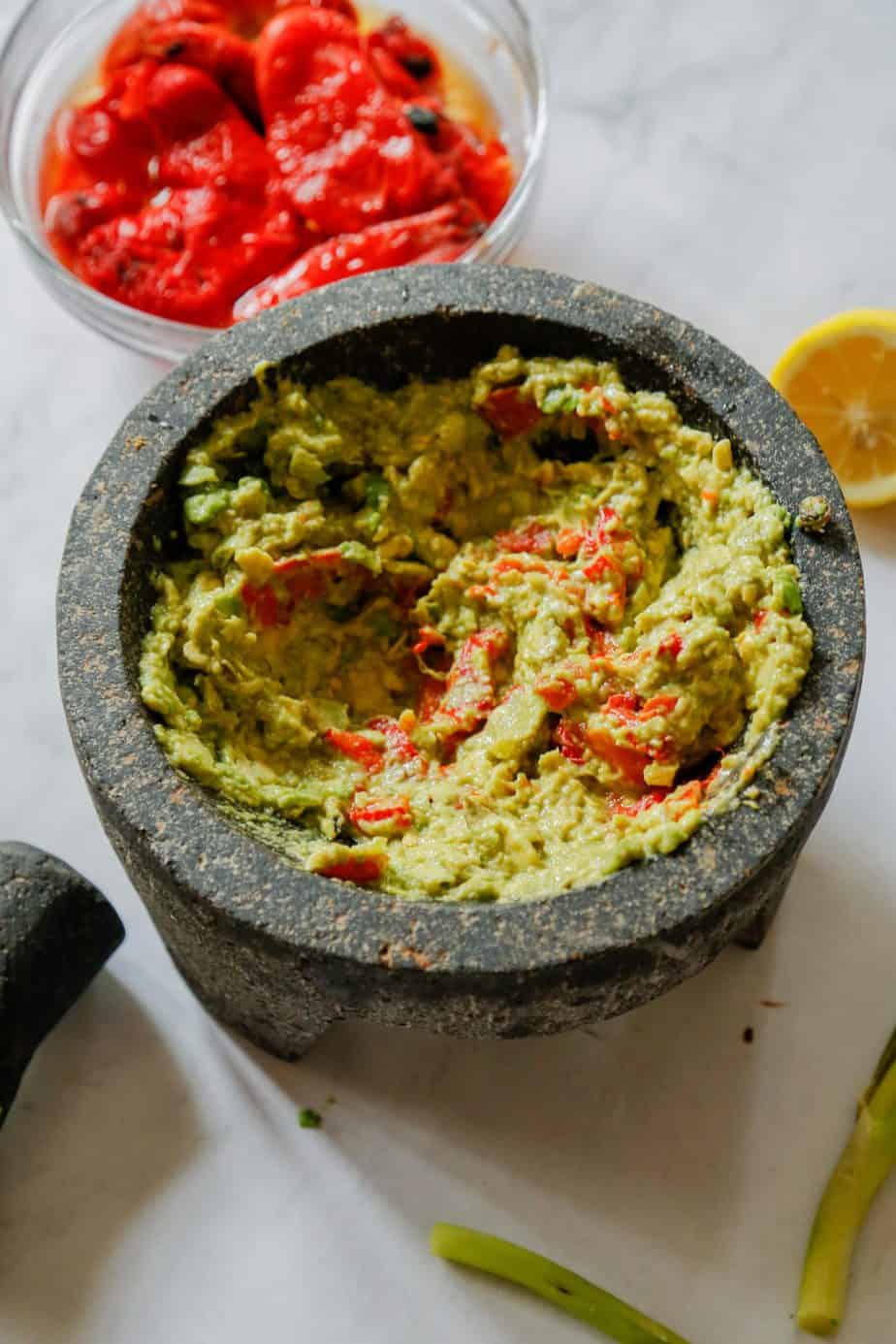 healthy guacamole with roasted red peppers scallions and cumin in a lava mortar and pestle