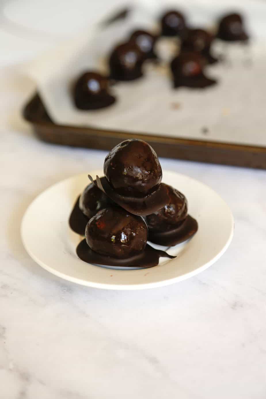 plate of vegan chocolate truffles with more truffles behind them on a sheet tray