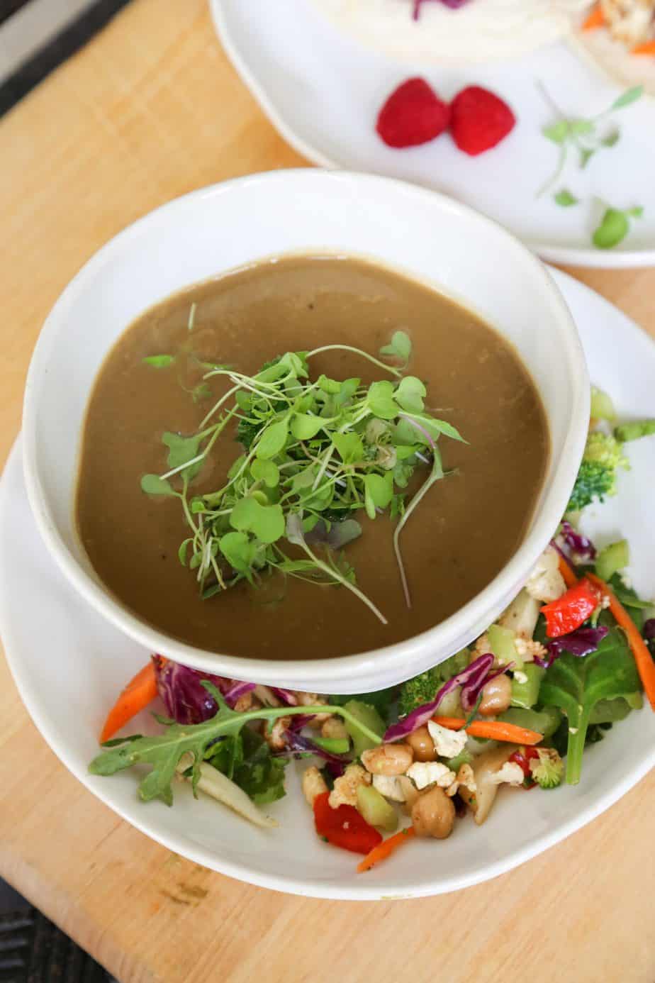 bowl of vegan and gluten free cream of mushroom soup with micro greens in a white bowl on a plate with salad