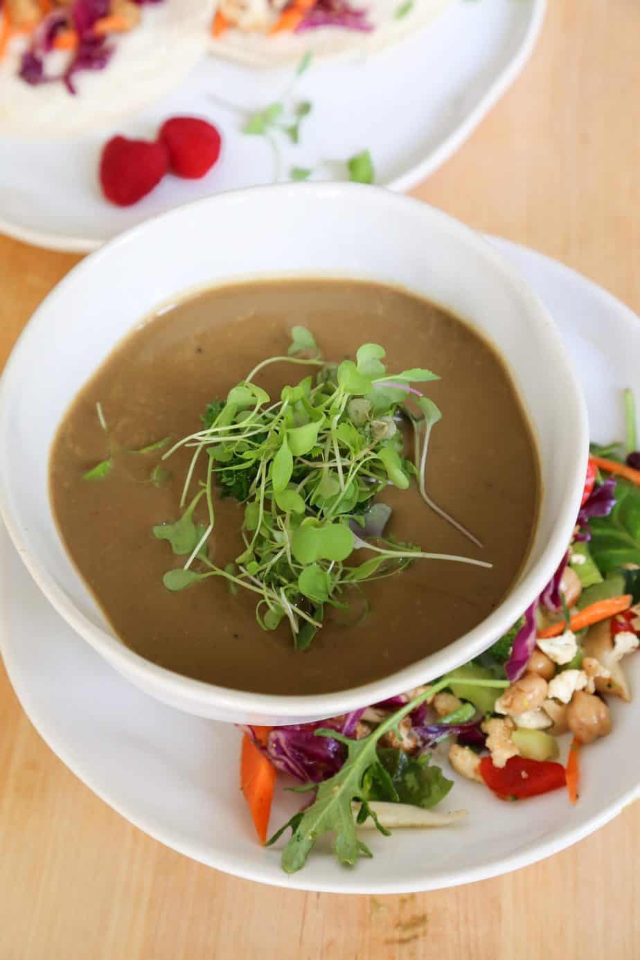 vegan mushroom soup in a bowl with micro greens and salad from above 