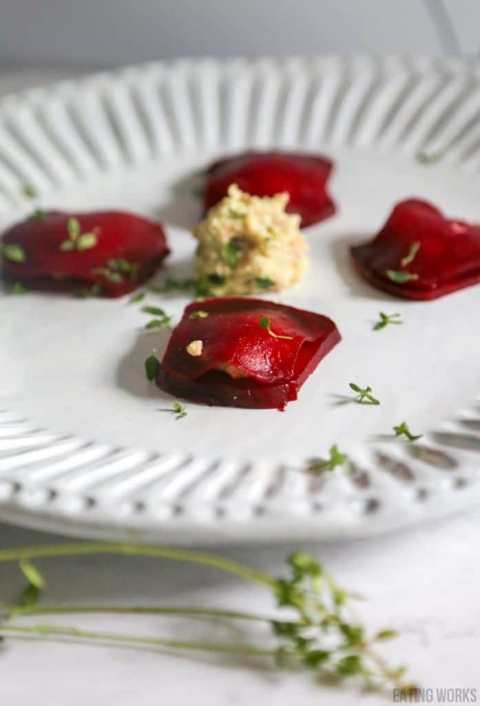 plate of beet ravioli with vegan ricotta on a white plate with thyme garnish