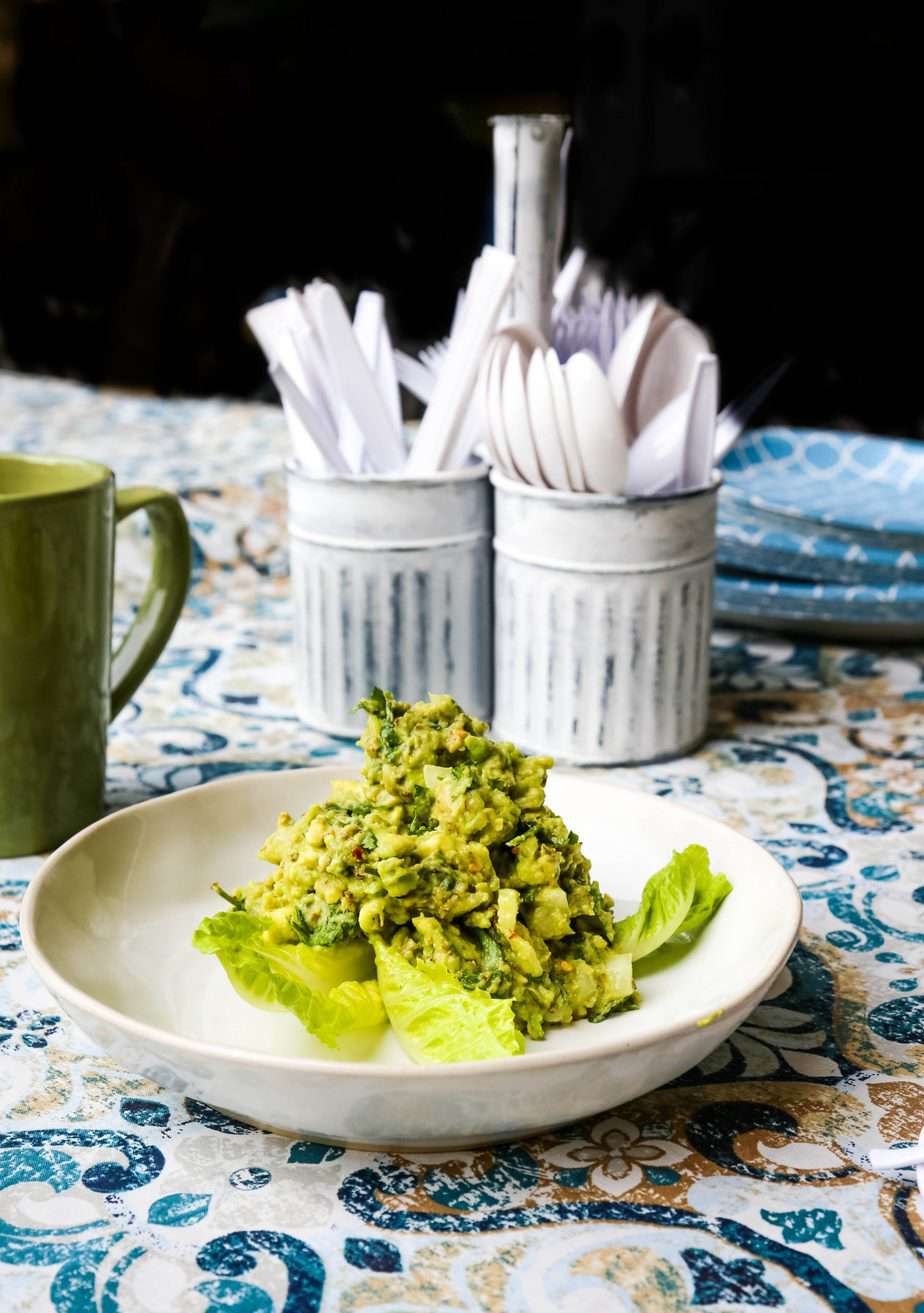 Healthy guacamole with cilantro and lime in a white Bowl on a blue table cloth 