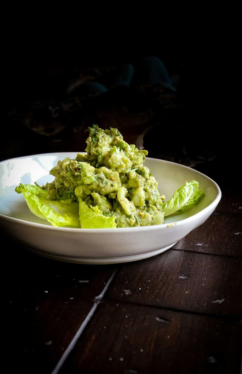 bowl of healthy guacamole with lemon and cilantro with lettuce leaves