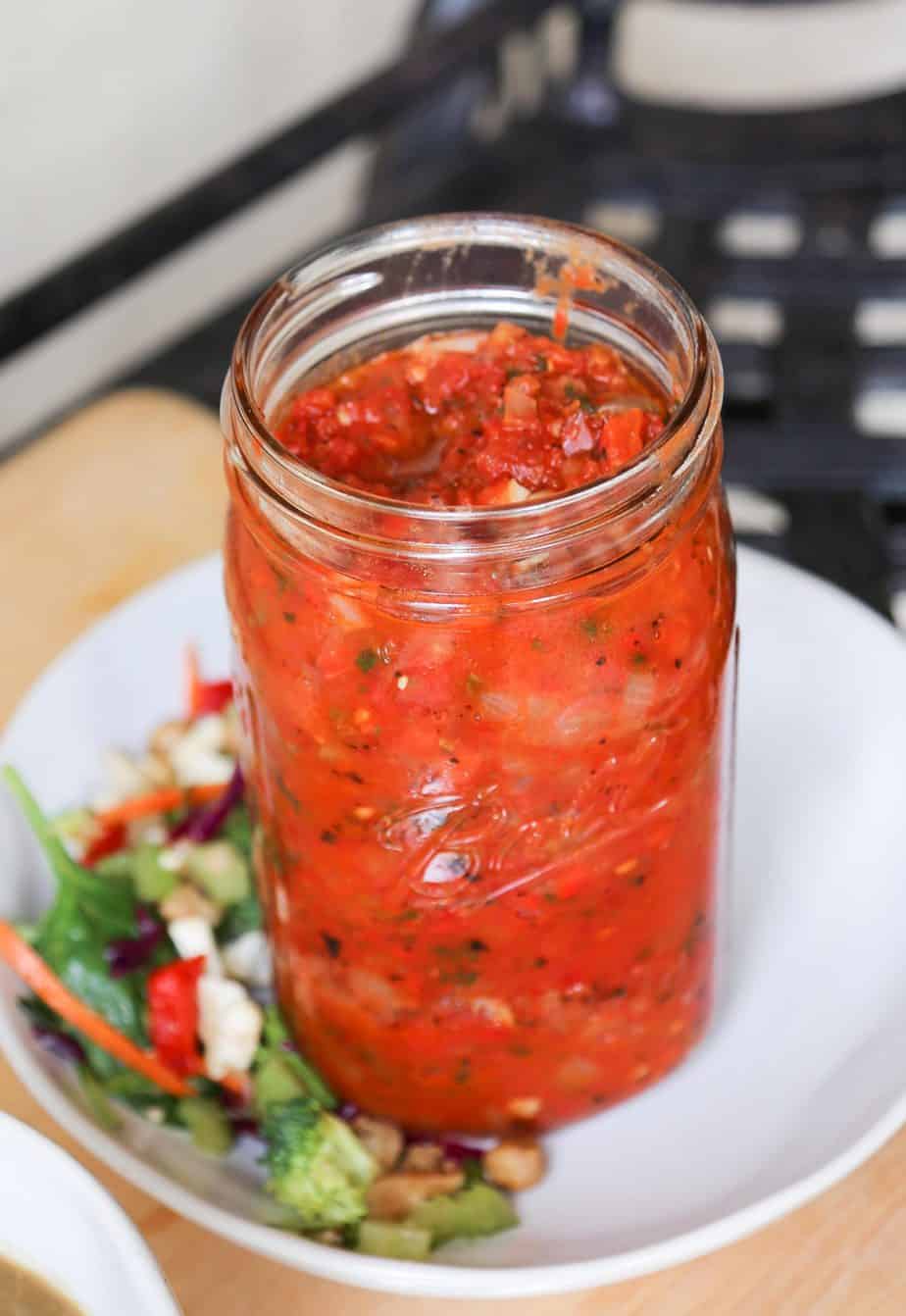 a jar of vegan roasted red pepper sauce on a white plate with vegetables