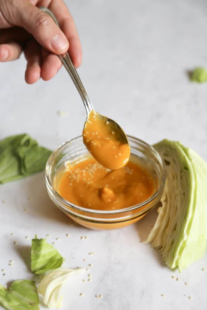 Carrot ginger miso dressing in a clear bowl and on a spoon