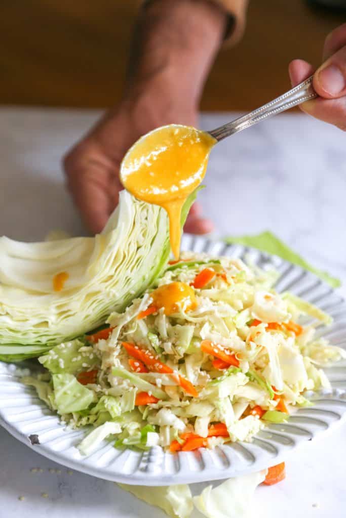 carrot cabbage ginger miso dressing dripping from a spoon onto a plate of cabbage and carrot salad