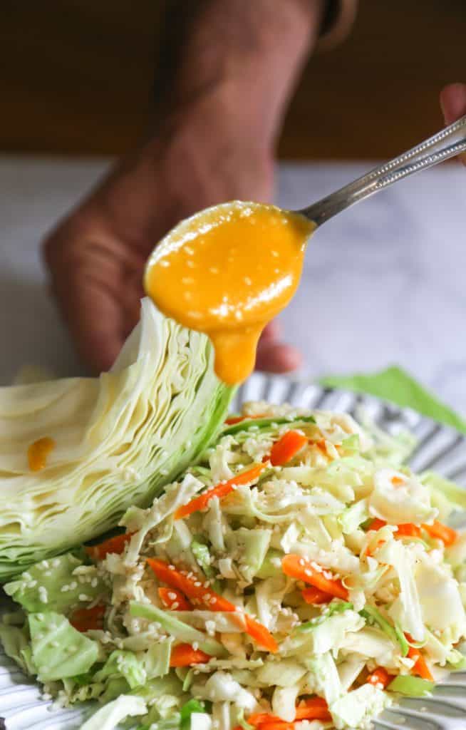 cabbage and carrot salad in a plate dressed with carrot ginger miso dressing from a spoon
