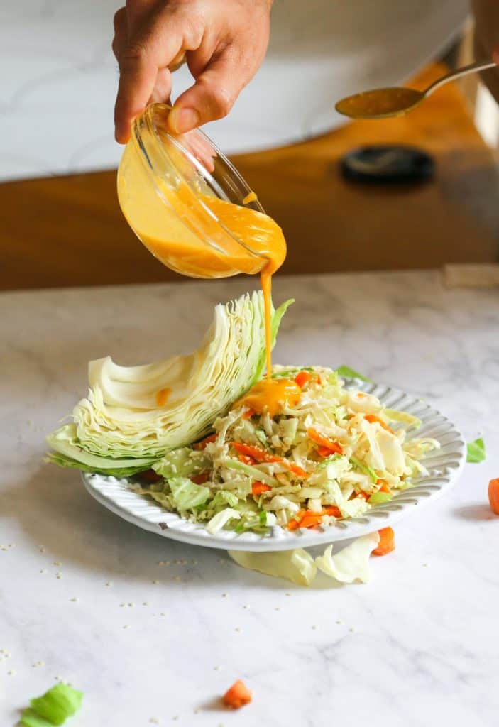 carrot and cabbage salad on a plate with carrot ginger miso dressing being poured on top