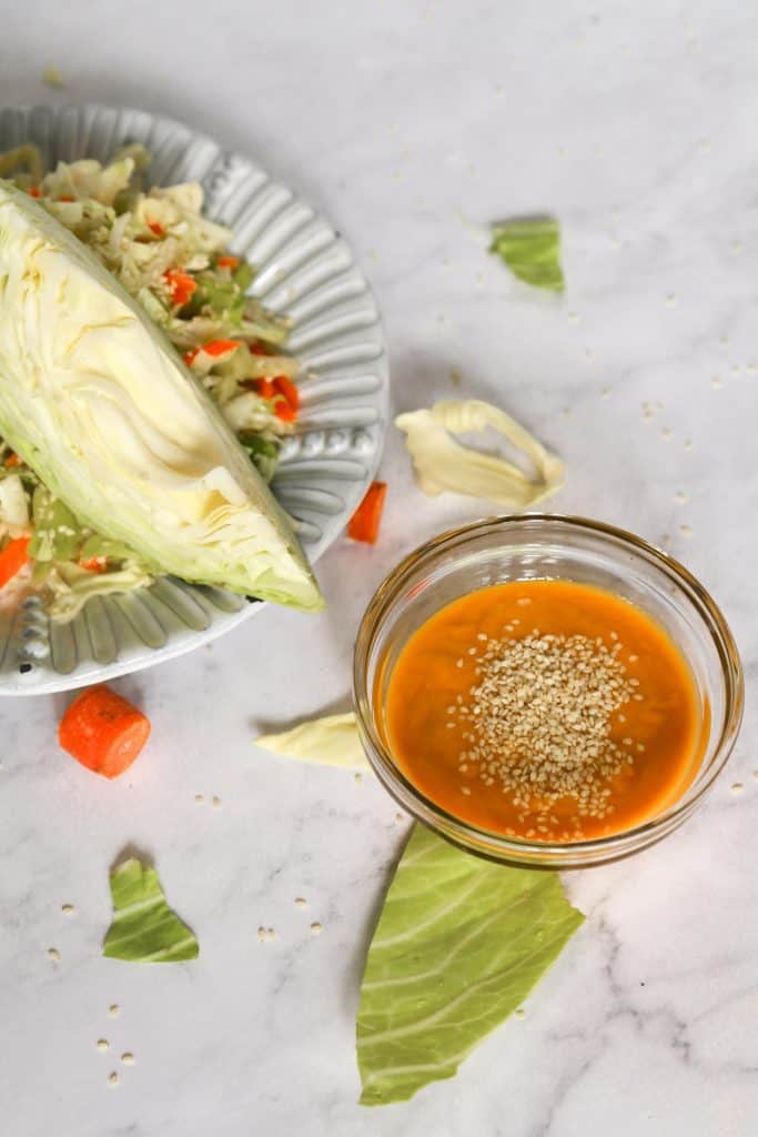 photo of cabbage and carrot salad from above with a bowl of carrot ginger miso dressing with sesame seeds 