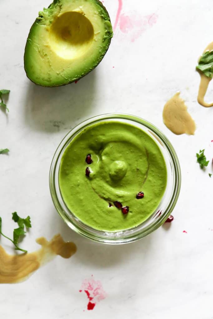 Green tahini sauce in a bowl from above next to an avocado