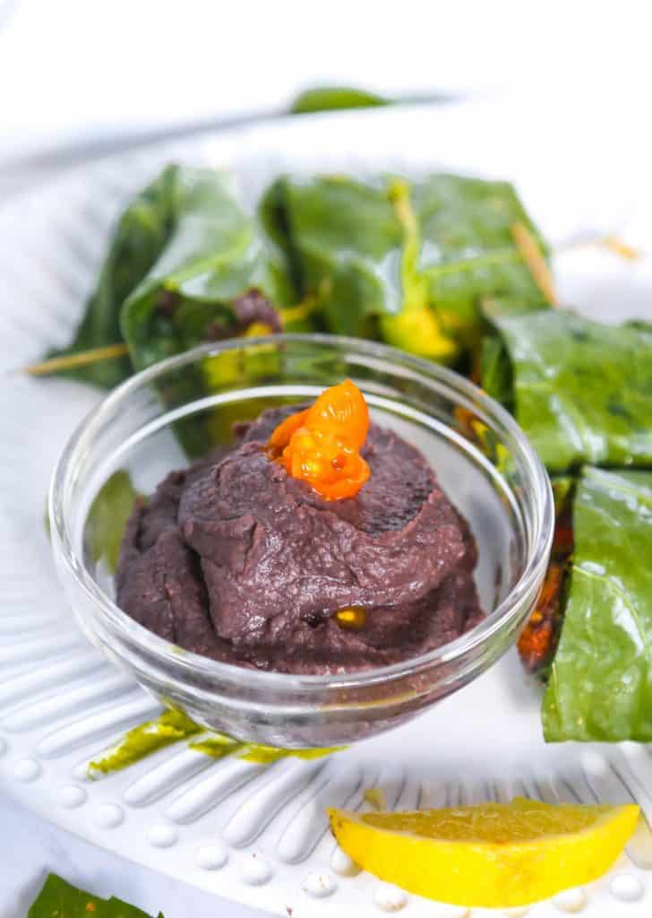 vegan refried black beans in a bowl surrounded by collard green wraps and topped with an orange tomato for garnish