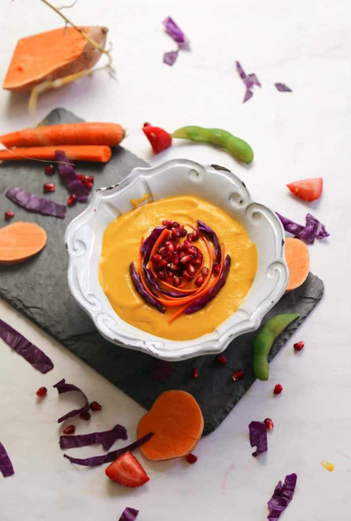 Carrot and orange soup with Sweet Potatoes in a white bowl made with sweet potato, carrots, apple ginger coconut milk and spices like cumin and cinnamon.