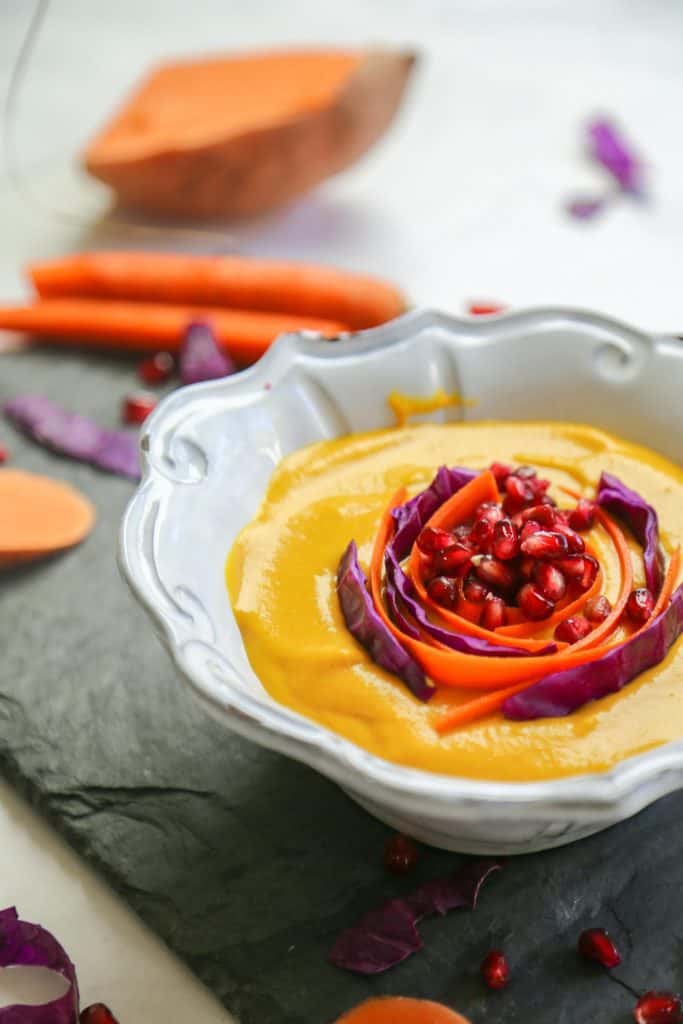 Carrot Ginger Soup with Sweet Potatoes in a white bowl made with sweet potato, carrots, apple ginger coconut milk and spices like cumin and cinnamon.