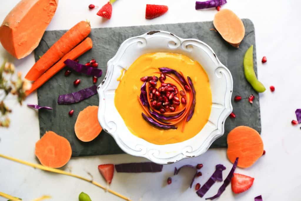 carrot and orange soup with Sweet Potatoes in a white bowl made with sweet potato, carrots, apple ginger coconut milk and spices like cumin and cinnamon.