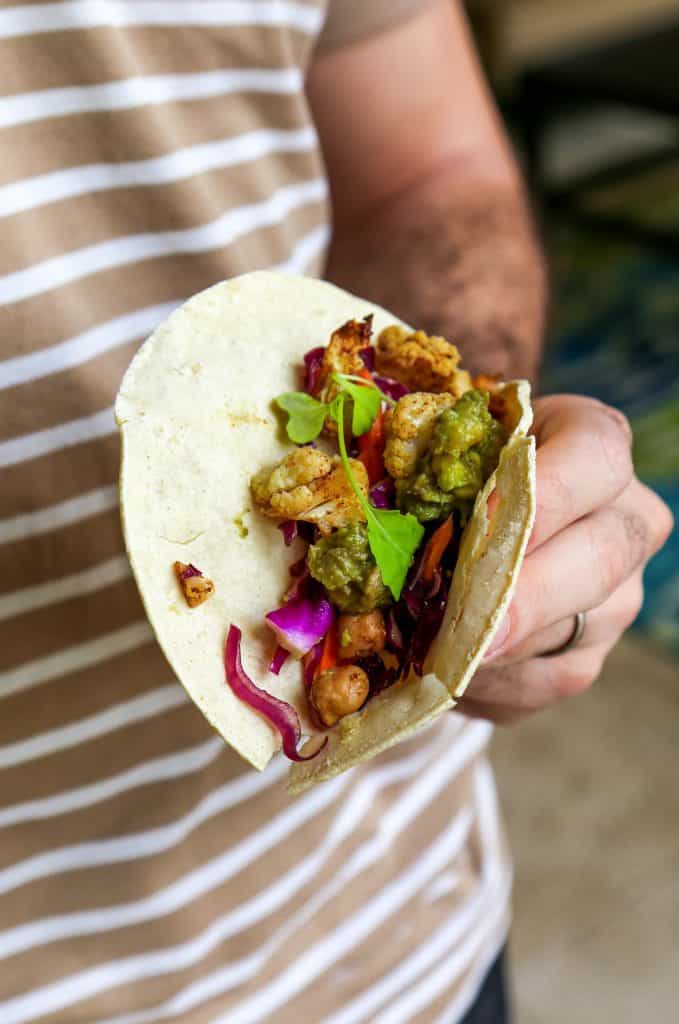 Chickpea Taco with cauliflower Avocado Crema and a cabbage and carrot slaw in a man's hand