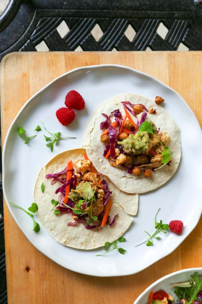 two vegan Chickpea Taco with cauliflower Avocado Crema and a cabbage and carrot slaw on a white plate