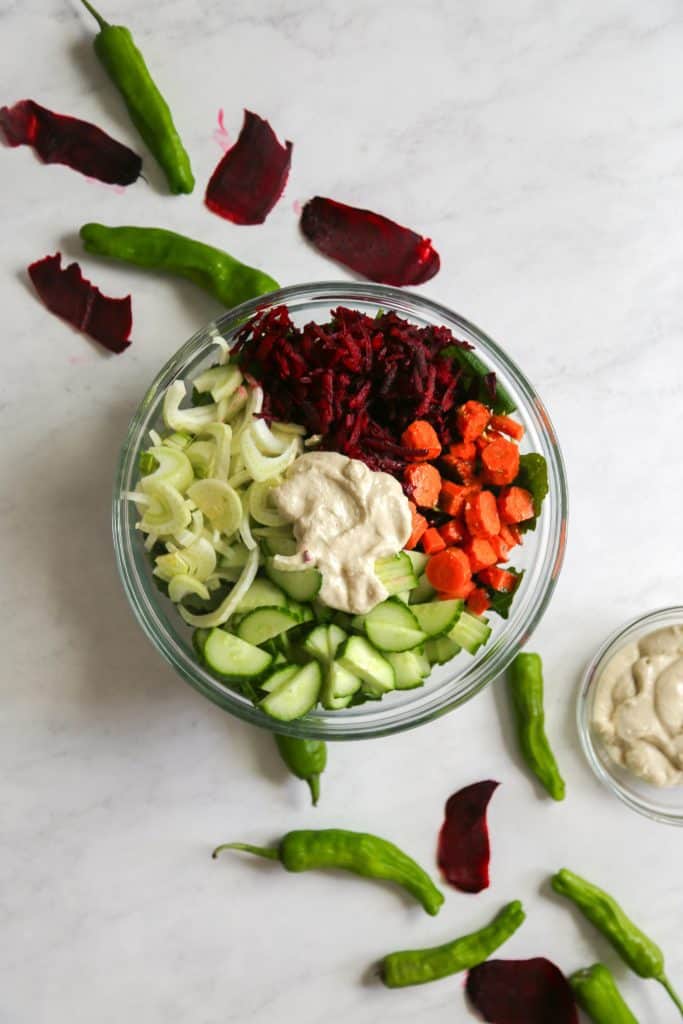 Kale salad with apple tahini dressing in a bowl from above with beets, cucumbers carrots fennel and a dollop of tahini apple dressing