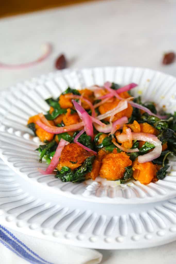 vegan grain free sweet potato gnocchi on a white plate with sautéed spinach with a blue napkin