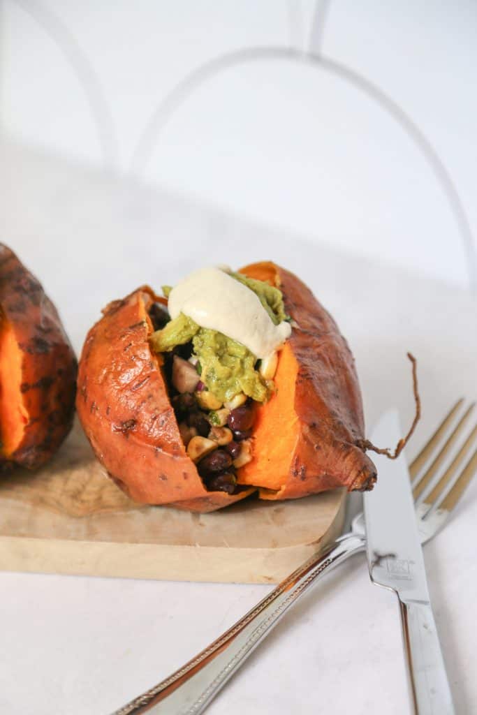 Vegan Stuffed Sweet Potato on a cutting board with guacamole, salsa and cashew cream