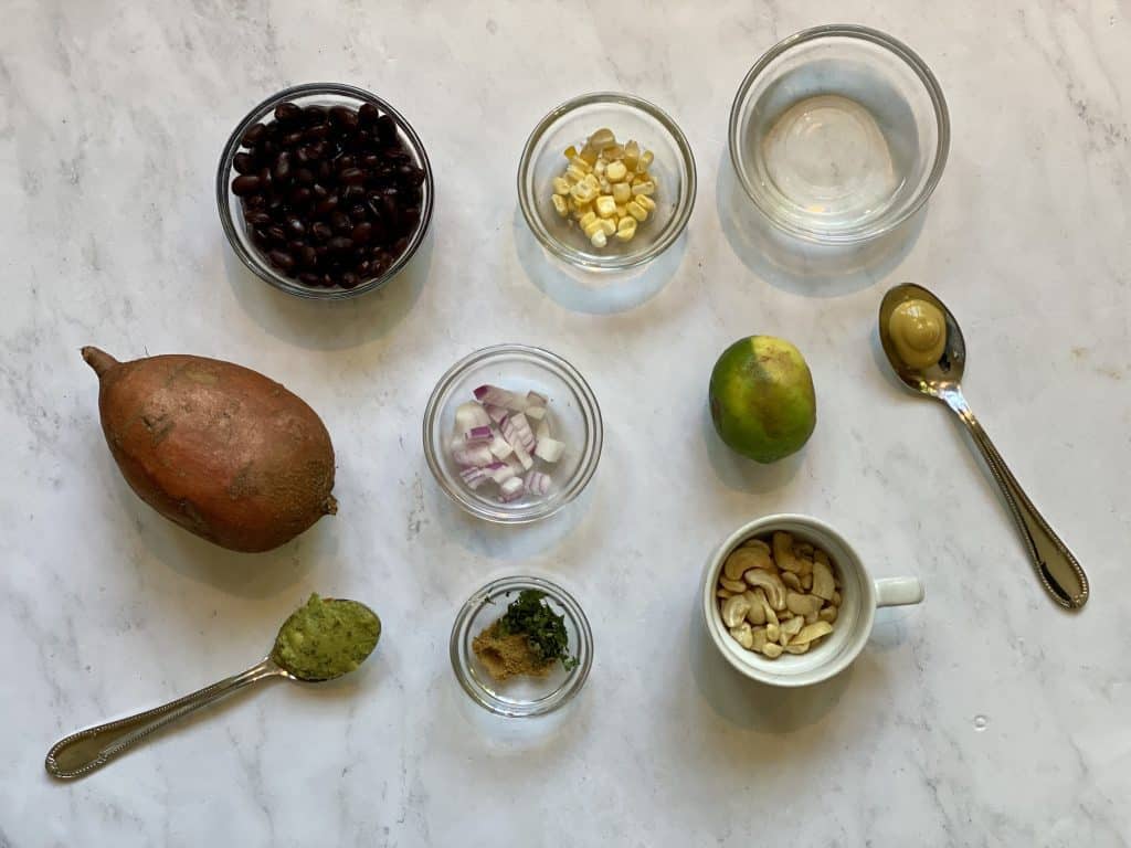 ingredients shown for vegan stuffed sweet potatoes, potatoes, black beans, corn, lime, cashews, cilantro, cumin, guacamole, vinegar, onions and mustard