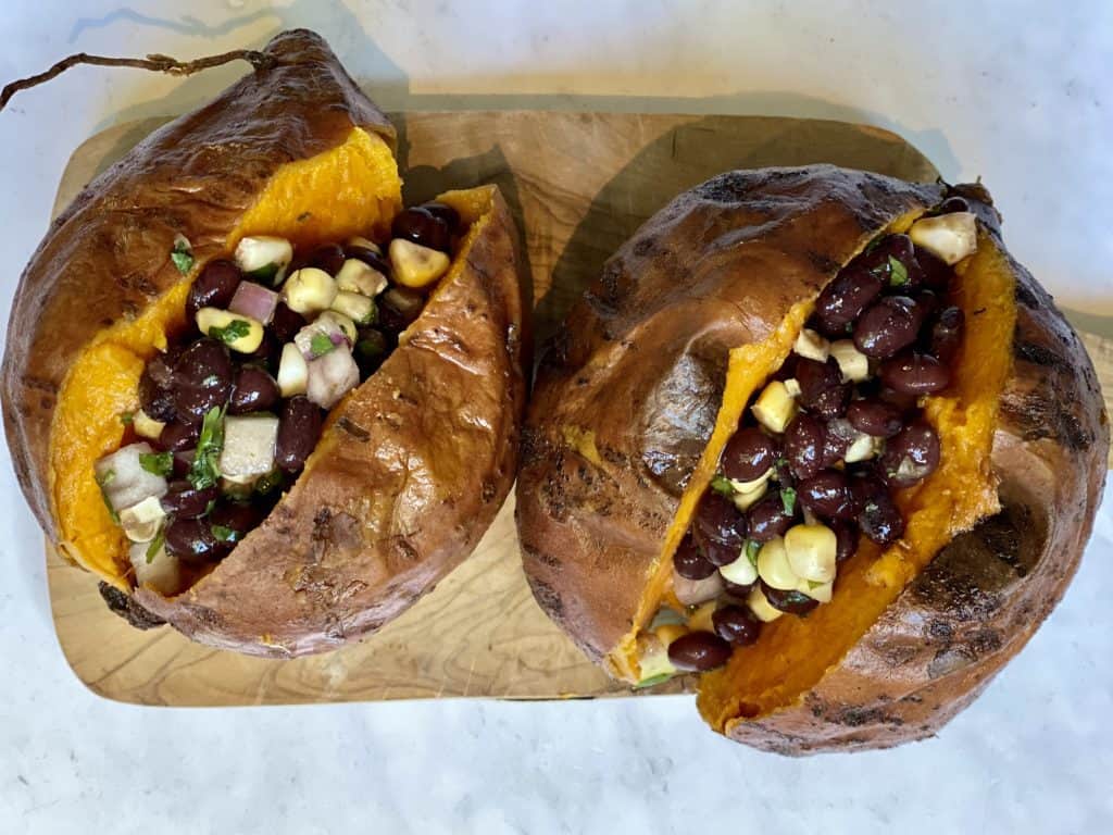 sweet potatoes cut open on a cutting board stuffed with black bean and corn salsa guacamole and cashew cream