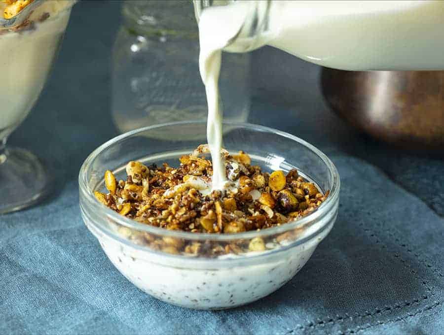 vegan keto breakfast granola in a bowl with milk being poured into it from above.