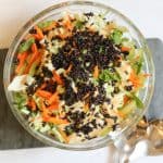 accompaniment salad with cabbage black rice sesame seeds carrots mint and ginger miso dressing in a glass serving bowl on a cutting board with serving spoons