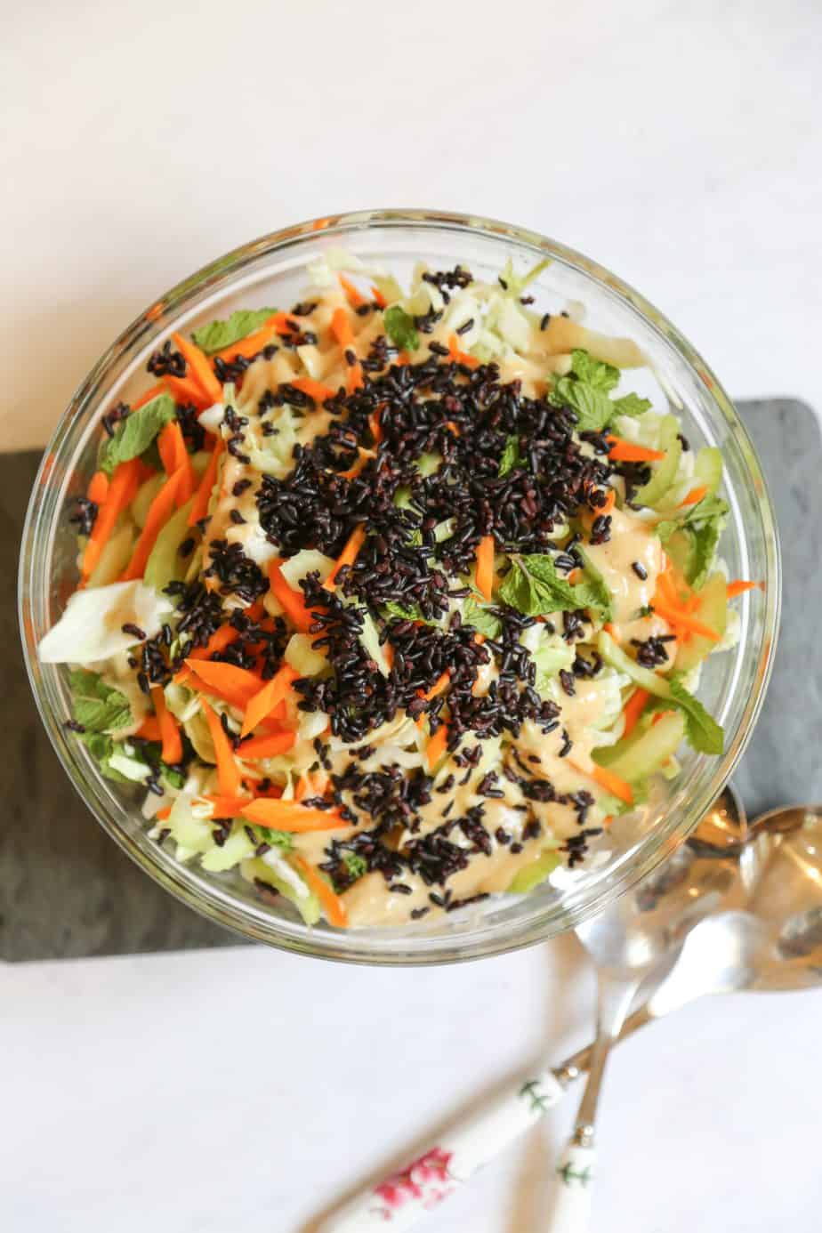accompaniment salad with cabbage black rice sesame seeds carrots mint and ginger miso dressing in a glass serving bowl on a cutting board with serving spoons 