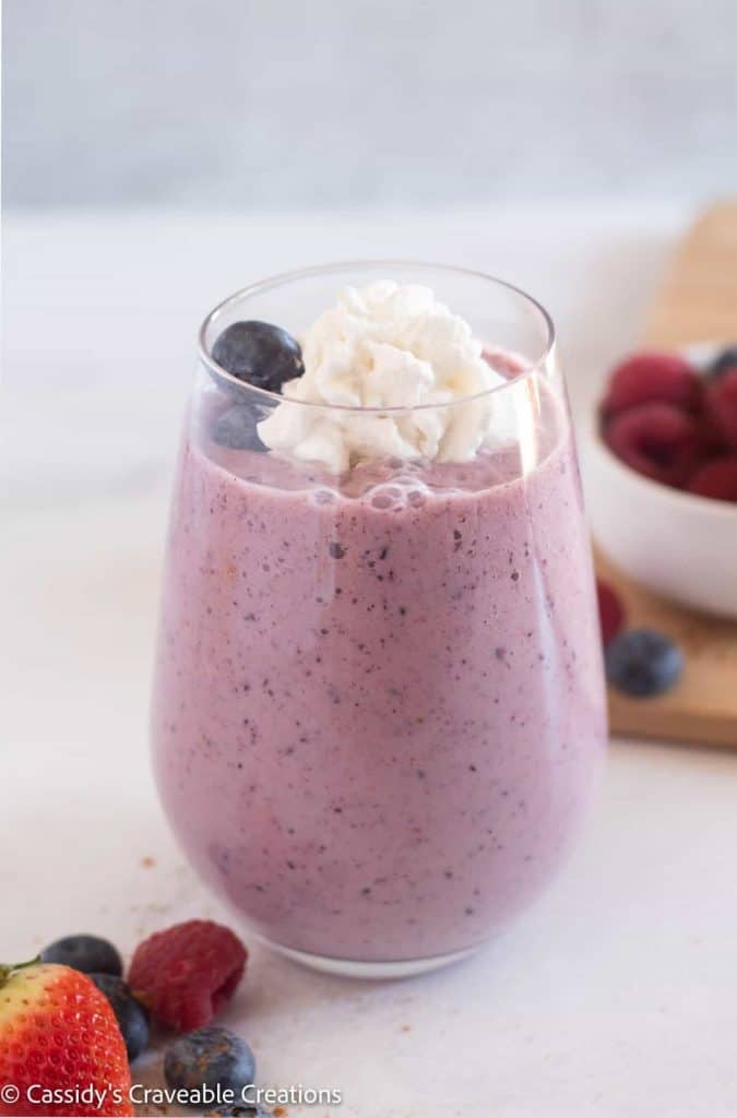 a pink berry smoothie in a glass with whip cream and berries.  Vegan Keto Breakfast Recipe