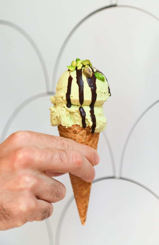 photo of vegan pistachio ice cream on a cone with chocolate drizzle and chopped pistachio nuts