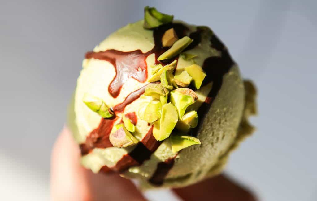 photo of vegan pistachio ice cream on a cone with chocolate drizzle and chopped pistachio nuts