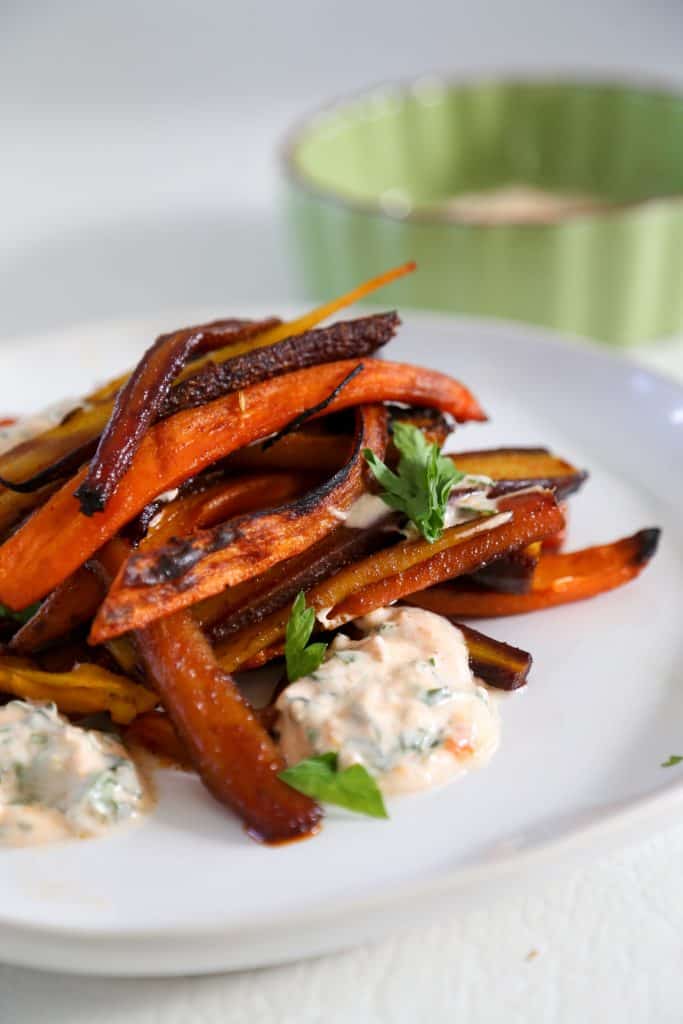 rainbow roasted carrots on a plate with harissa yogurt sauce.