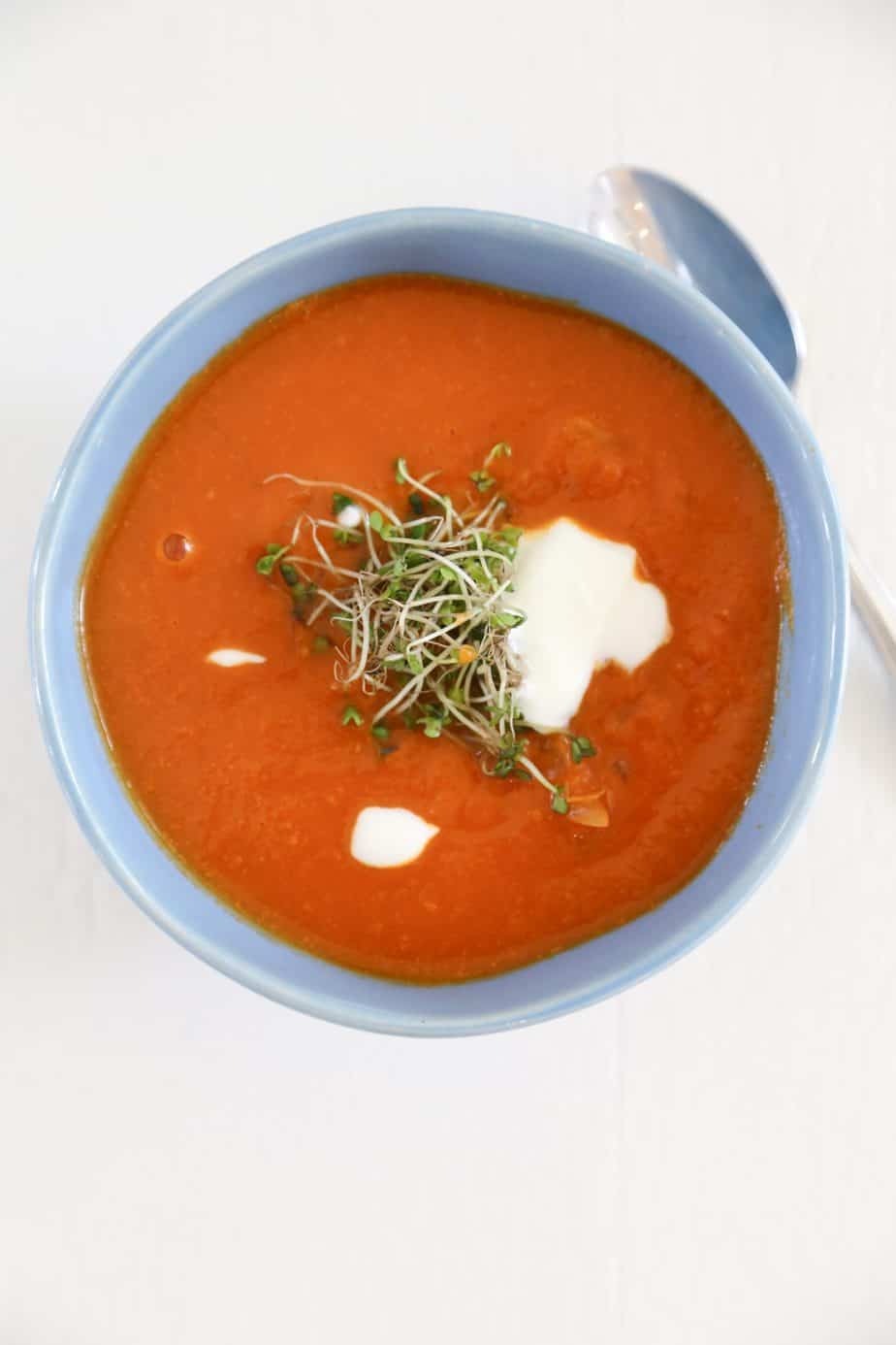 Gluten free tomato soup in a blue bowl with microgreens.
